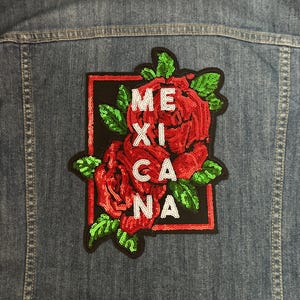 May include: A red, white, and black embroidered patch with the word "MEXICANA" in white letters surrounded by red roses. The patch is sewn onto a blue denim jacket.