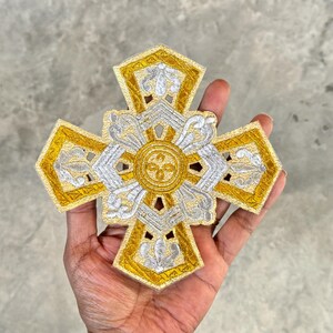 Puede incluir: Una cruz bordada en oro y plata con intrincados diseños florales. La cruz es un símbolo religioso y se utiliza a menudo en la decoración de las iglesias.