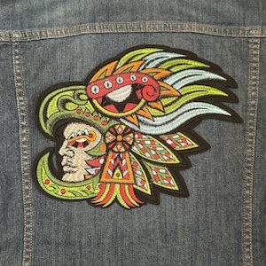 May include: Embroidered patch featuring a colorful, stylized depiction of a person's head wearing a headdress with feathers and geometric patterns. The colors include green, red, orange, yellow, and blue.