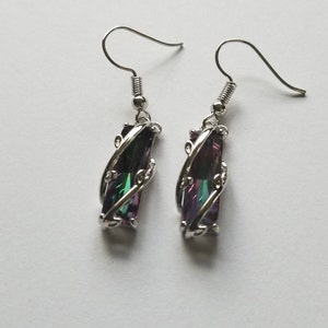 May include: Silver dangle earrings with a long, rectangular iridescent gemstone set in a silver swirl design.