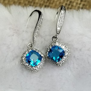 May include: A pair of silver dangle earrings with a square blue gemstone surrounded by smaller clear gemstones.