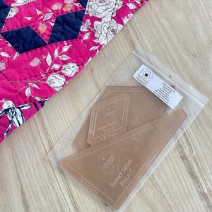 May include: A pink floral quilt with a star pattern and a clear plastic bag containing acrylic quilt templates. The templates are labeled "Sweet Selah" and "Piece A" and "Piece C" with 3/8" seam measurements. The quilt has a floral design.