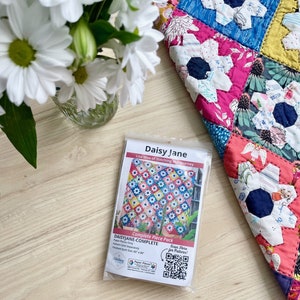 May include: A complete piece pack for a quilt pattern called Daisy Jane by Lisa Siva of Stitching the Journey. The pack includes all the fabric pieces needed to make a 60" x 60" quilt. The quilt features a colorful daisy design with pink, blue, yellow, and white flowers.