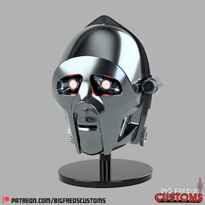 May include: A silver robot head with red glowing eyes on a black stand. The head has a detailed design with gears and a mouth.