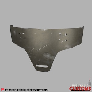 May include: A silver-colored metal face mask with a textured surface and multiple holes. The mask has a curved top and a pointed bottom.