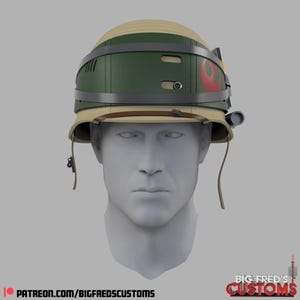 Puede incluir: Un casco beige y verde con una visera y detalles en gris oscuro. El casco presenta un emblema rojo y naranja en el lateral y una pequeña luz en el lado derecho. Es una réplica de un casco de Star Wars.