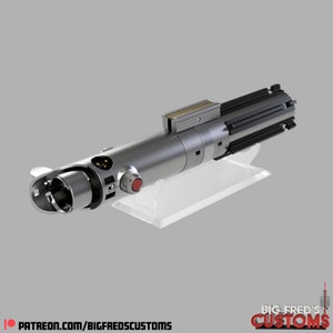 May include: A silver lightsaber with a black handle and a red button. The lightsaber is on a clear plastic stand. The text "BIG FRED'S CUSTOMS" is visible in the lower right corner of the image.