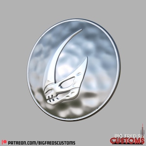 Könnte beinhalten: Ein silberfarbenes Emblem mit einem stilisierten Schädeldesign in einem kreisförmigen Rahmen. Das Emblem hat eine glänzende Oberfläche und ist vor einem grauen Hintergrund platziert. Der Text "PATREON.COM/BIGFREDSCUSTOMS" befindet sich unten.