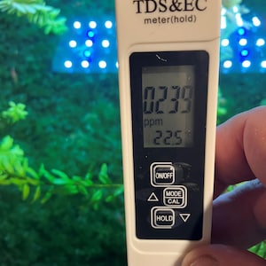 Puede incluir: Un medidor blanco de TDS y EC con una pantalla digital que muestra una lectura de 0239 ppm y 22,5. El medidor tiene botones para encendido/apagado, modo, calibración y retención.