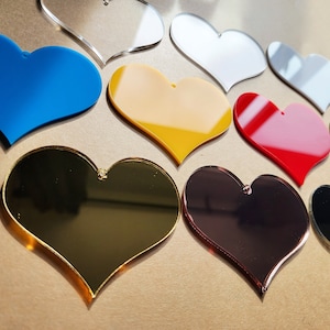 May include: Assortment of heart-shaped acrylic ornaments in various colors, including blue, yellow, red, gold, silver, and black. The ornaments are all the same size and shape, and they are arranged in a random pattern.