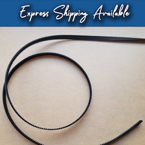 May include: A black rubber timing belt with teeth, lying on a brown surface.