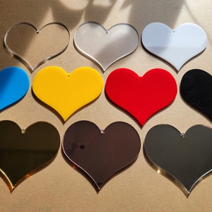 May include: Ten heart-shaped acrylic blanks in various colors, including clear, white, black, blue, red, yellow, gold, and silver. The blanks are perfect for crafting and personalization.