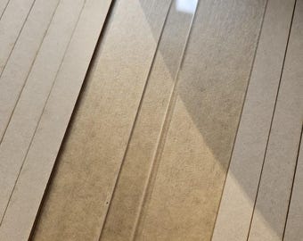 May include: A clear, rectangular acrylic strip is positioned diagonally, surrounded by several light brown, rectangular wooden strips. The acrylic strip reflects light, contrasting with the matte finish of the wood. The items are arranged on a neutral-toned surface.