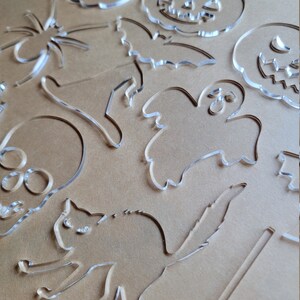 May include: A set of clear acrylic Halloween-themed cutouts, including a ghost, a cat, a spider, a bat, a skull, a pumpkin, and a witch's hat.