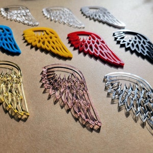 May include: Assortment of colorful acrylic angel wings in various designs. The wings are translucent and have a delicate, intricate pattern. The colors include blue, yellow, red, pink, and clear.