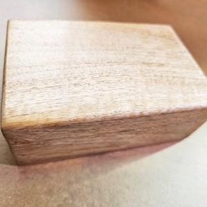 May include: A rectangular wooden box with a light brown finish. The box has a simple, clean design with visible wood grain. The edges are slightly rounded, giving it a smooth appearance. The box is likely used for storage or display.
