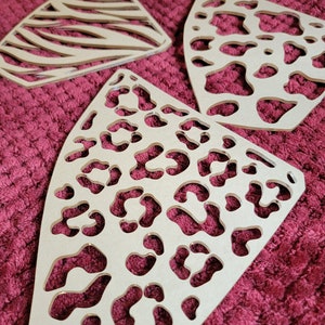 May include: Three beige wooden cutouts with animal print designs. The cutouts are shaped like a triangle with rounded edges. The designs are zebra stripes, leopard spots, and cheetah spots.