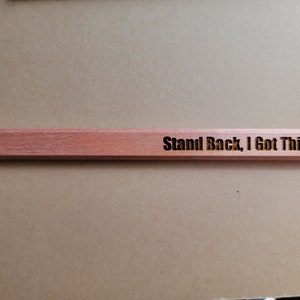 Puede incluir: Una regla de madera con el texto "Stand Back, I Got This" grabado en ella.