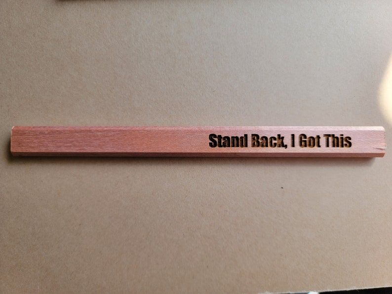 Puede incluir: Una regla de madera con el texto "Stand Back, I Got This" grabado en ella.