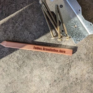 Puede incluir: Una placa de madera con las palabras "Father, Grandfather, Hero" grabadas en ella. La placa es de color marr&oacute;n claro y tiene una forma ligeramente redondeada.