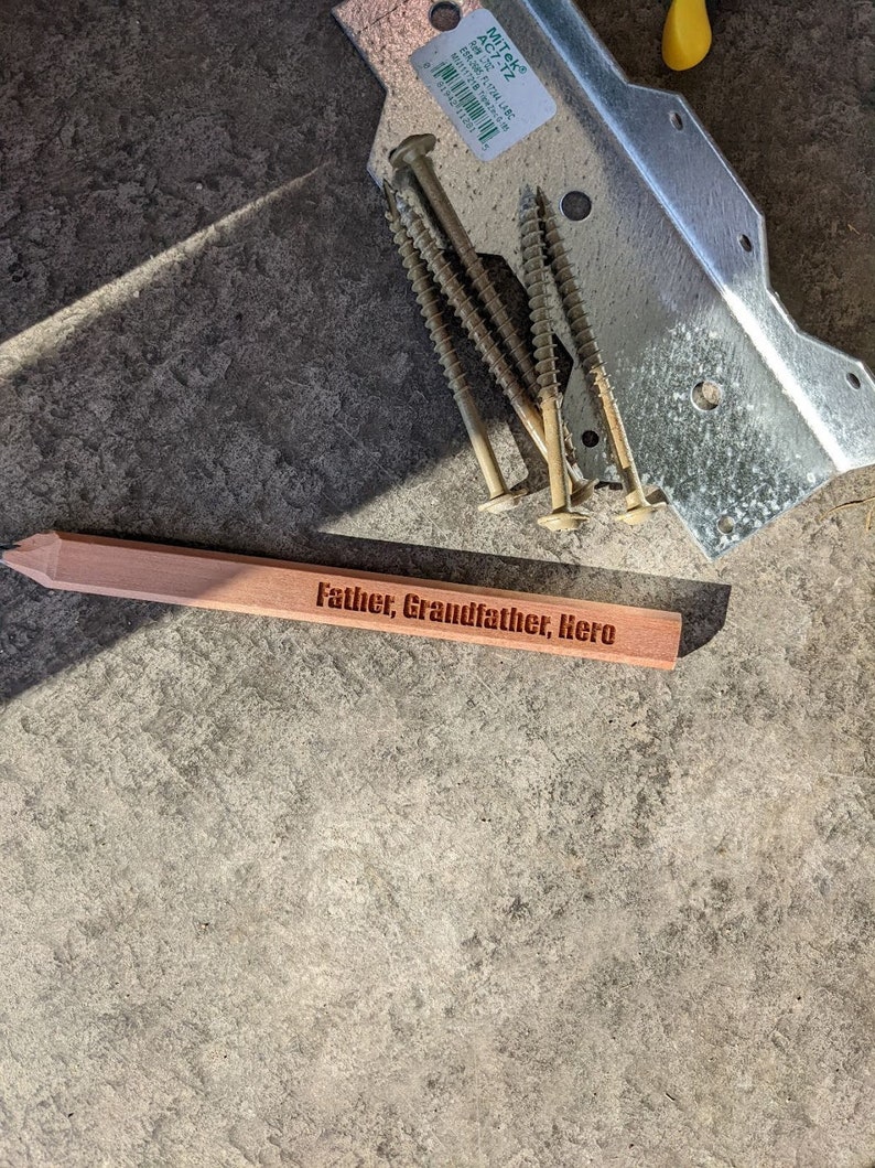 Puede incluir: Una placa de madera con las palabras "Father, Grandfather, Hero" grabadas en ella. La placa es de color marr&oacute;n claro y tiene una forma ligeramente redondeada.