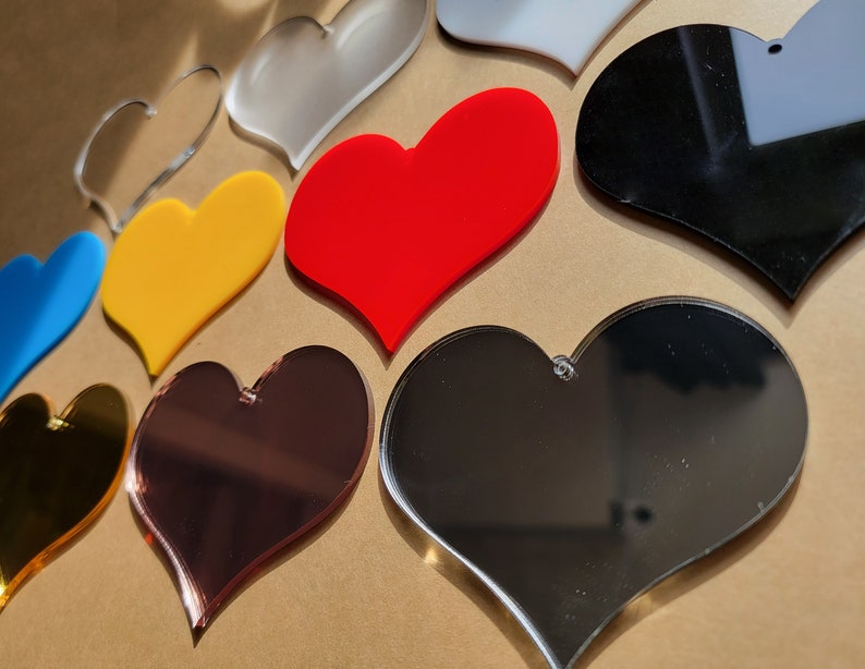 May include: Assortment of heart-shaped acrylic blanks in various colors, including red, yellow, blue, black, gold, and silver. The hearts are all approximately the same size and have a smooth, glossy finish.