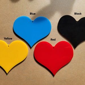 May include: Four heart-shaped acrylic ornaments in different colors: yellow, blue, red, and black. Each ornament has a small hole at the top for hanging.
