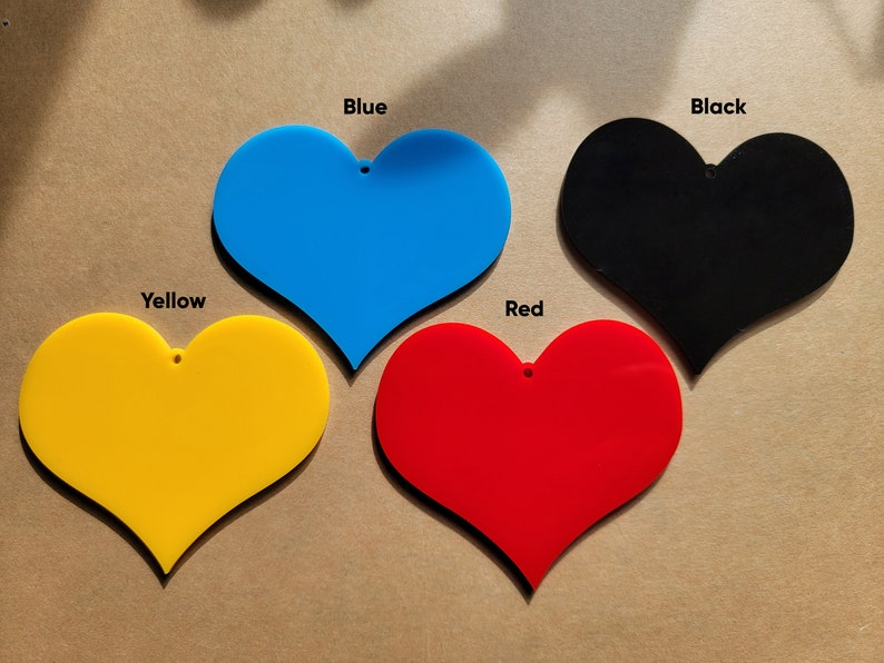 May include: Four heart-shaped acrylic ornaments in different colors: yellow, blue, red, and black. Each ornament has a small hole at the top for hanging.