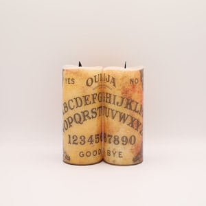 Vela de cera de LED inspirada em um tabuleiro Ouija, operada por bateria, com chama preta e opção de controle remoto. Invoque espíritos ou decore para o Halloween.