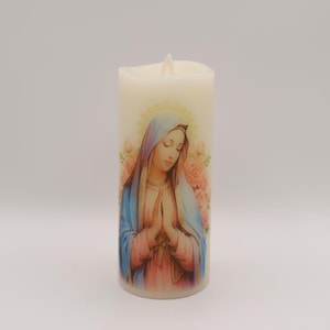 Può includere: Una candela a LED color crema con l'immagine della Vergine Maria con velo blu, veste rosa e aureola dorata. La candela ha un effetto fiamma tremolante ed è circondata da rose rosa.