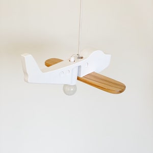 May include: White wooden airplane pendant light with a natural wood propeller. The light is hanging from a white cord.