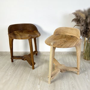 May include: Two wooden stools with unique, handcrafted designs. The stools are made of natural wood with a warm brown finish. The stools have a simple, yet elegant design, making them perfect for adding a touch of rustic charm to any space.