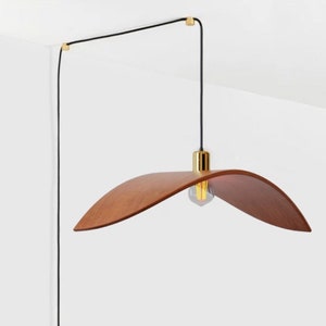 Könnte beinhalten: Eine Holz-Pendelleuchte mit einem geschwungenen, braunen Holzschirm und einer goldenen Metallfassung. Die Leuchte wird mit einem schwarzen Kabel von der Decke abgehängt.