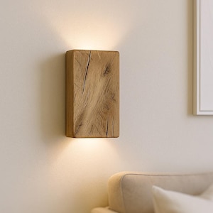Op de afbeelding: Een rechthoekige houten wandlamp met een natuurlijke houtnerf. Gemonteerd op een lichtgekleurde muur, straalt het warm licht naar beneden. Het ontwerp is rustiek en modern, geschikt voor binnenverlichting.