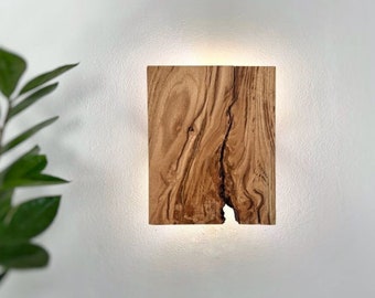 May include: A wall-mounted light fixture made from a piece of natural wood with a unique grain pattern. The light fixture is illuminated, casting a warm glow.