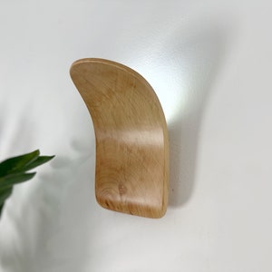 Op de afbeelding: Een lichte houten wandhaak met een gebogen ontwerp.