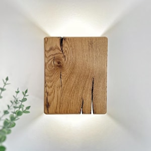Könnte beinhalten: Eine quadratische Wandleuchte aus Holz mit einem warmen Licht, das von hinten durch das Holz scheint. Das Holz hat ein natürliches, rustikales Aussehen mit Knoten und Maserungen.