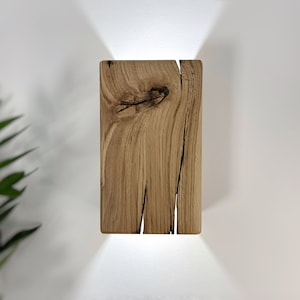 May include: A rustic wooden wall sconce with a natural wood finish and a rectangular shape. The sconce has a unique, knotty grain pattern and a light shining through the wood.