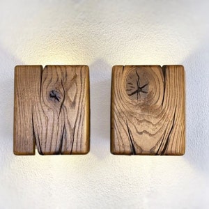 May include: Two rustic wooden wall sconces with a warm, natural wood finish. The sconces have a simple, rectangular shape and feature a knot in the wood.