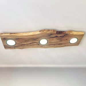 May include: A wooden ceiling light fixture with a natural wood finish and three round light bulbs.