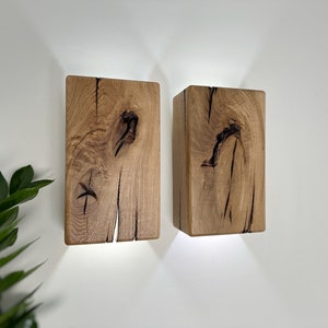 May include: Two rustic wooden wall sconces with a warm, natural wood finish. The sconces have a rectangular shape and feature a unique, knotty wood grain pattern.