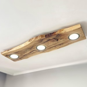 May include: A ceiling light fixture made from a natural wood slab with a rough, organic edge. The fixture has three integrated LED lights.