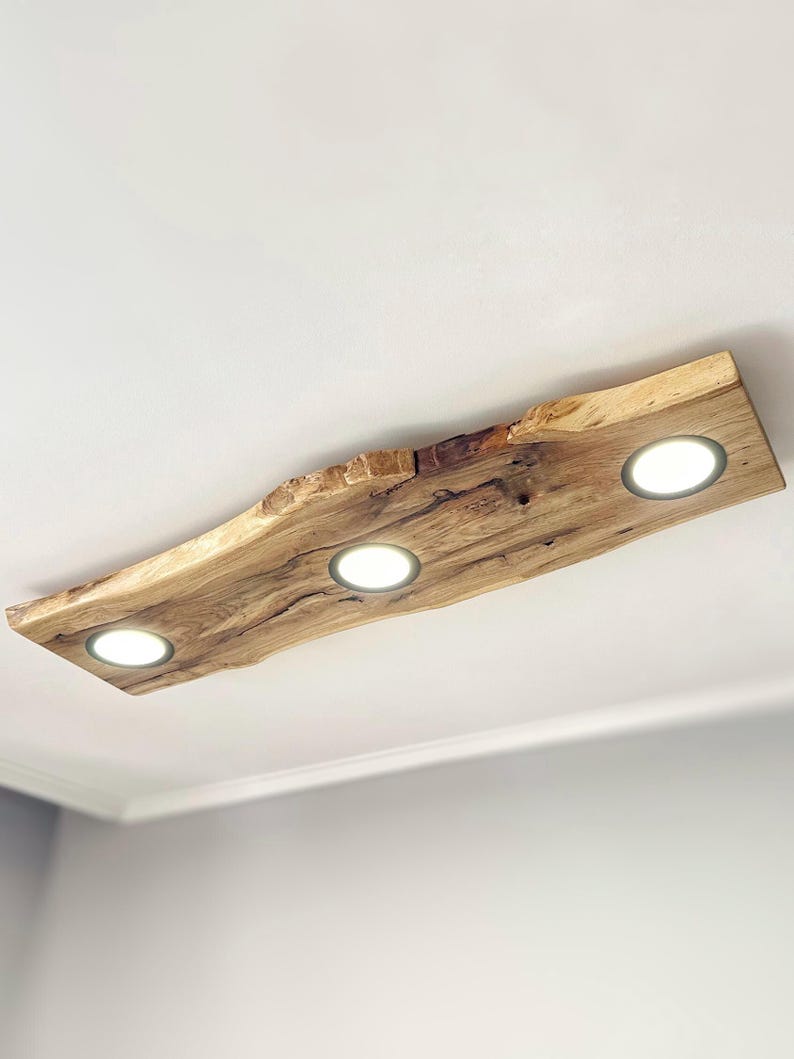 May include: A ceiling light fixture made from a natural wood slab with a rough, organic edge. The fixture has three integrated LED lights.
