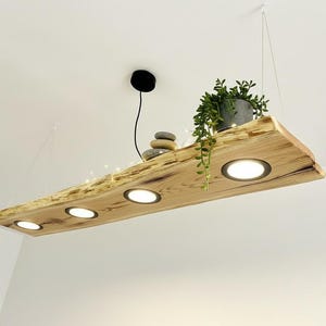 May include: A rustic wooden light fixture with four recessed lights. The light is suspended from the ceiling and features a live edge design. A small potted plant and decorative stones sit on top. Fairy lights are strung along the wood.