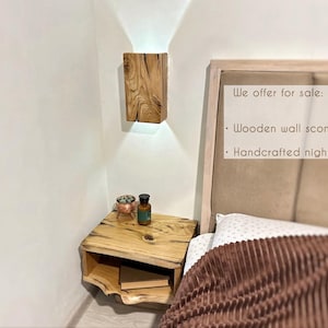 May include: A wooden nightstand with a shelf and a small wooden wall sconce above it. The nightstand is next to a bed with a brown blanket. The text on the headboard reads: "We offer for sale: Wooden wall sconce Handcrafted nightstand"