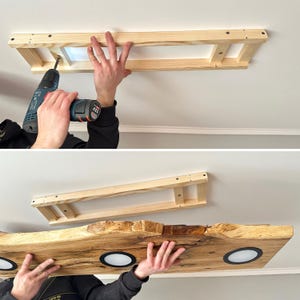 May include: A wooden frame is being attached to the ceiling with a drill. The frame will be used to support a wooden shelf with integrated lights. The shelf is made of a natural wood with a live edge and has three round lights.