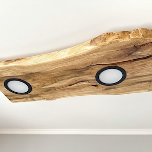May include: A wooden ceiling light fixture with a natural wood finish and two round white lights with black bezels.