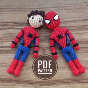 May include: Two crocheted Spiderman dolls, one with a brown hair and a face, the other with a red and blue Spiderman mask. The dolls are laying on a wooden surface with the text "PDF PATTERN" in a circle.