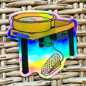 May include: A colorful sticker of a pottery wheel with a foot pedal. The wheel is gold with a blue base and the foot pedal is brown with a checkered pattern. The sticker has a holographic finish.