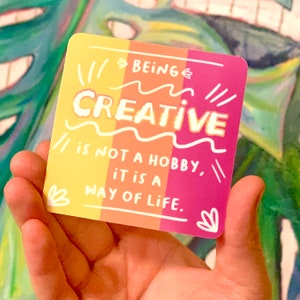 May include: A yellow, orange, and pink sticker with the text "BEING CREATIVE // is not a hobby, it is a WAY OF LIFE."